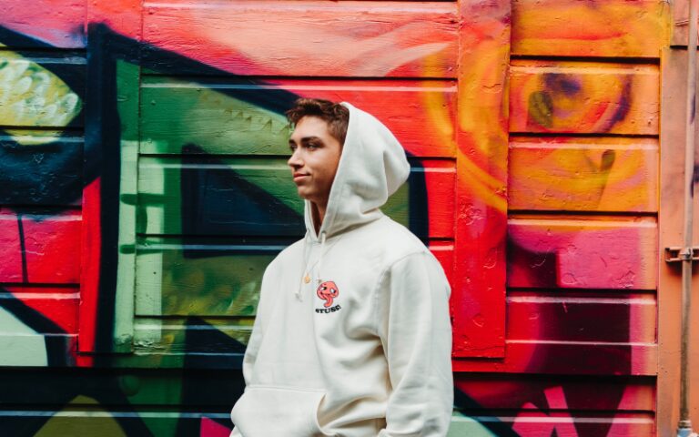 A man in white hoodie standing next to colorful wall.